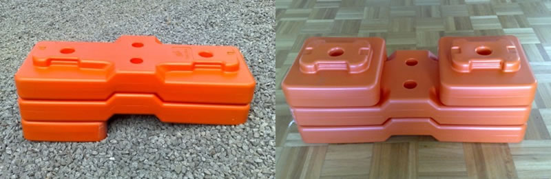 Two orange blow molded temporary fence feet on the ground. They all consist of two or three parts.